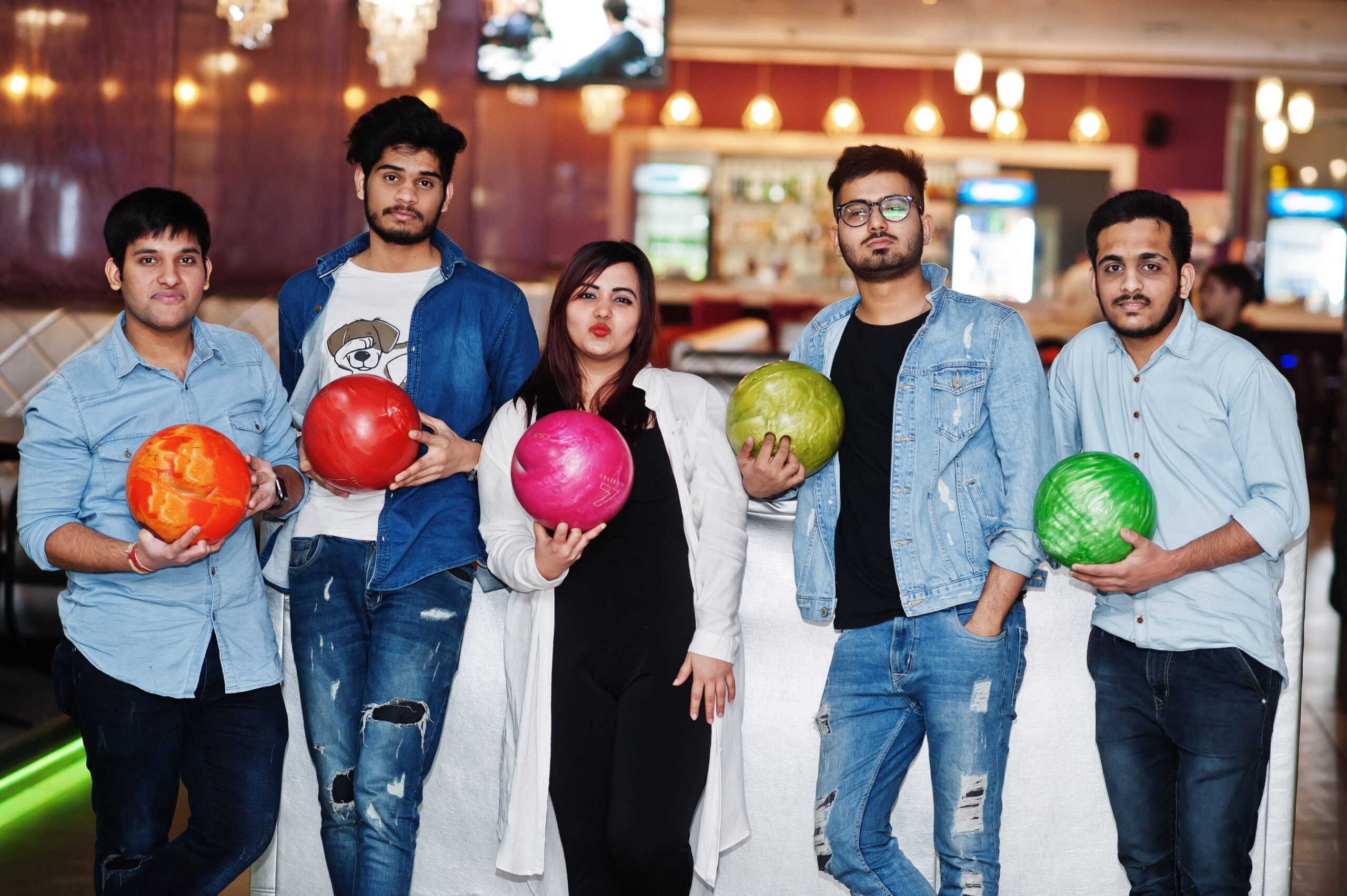 Group of five south asian peoples having rest and fun at bowling club with balls at hands.