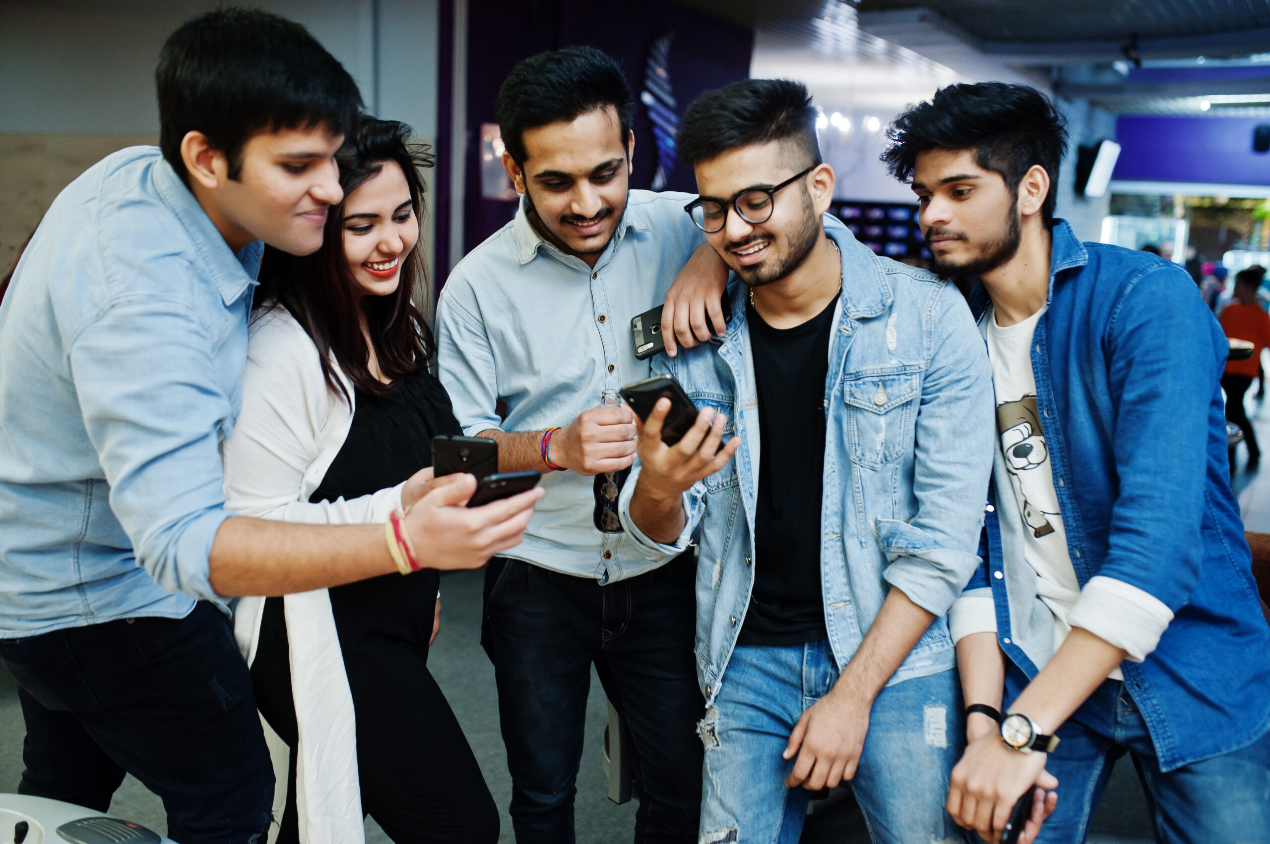 Group of stylish asian friends wear on jeans looking at mobile phones in club.